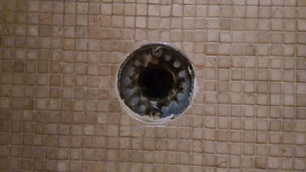 Marble shower floor with build-up on drain.